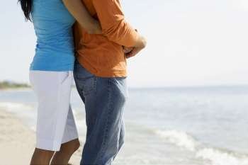 Mid section view of a woman embracing a man from behind on the beach