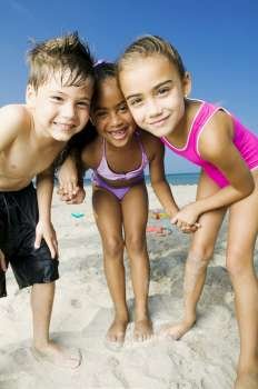 Portrait of two girls and a boy standing on the beach and smiling