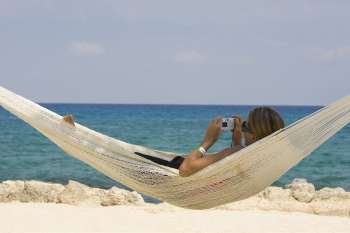 Young woman lying in a hammock and holding a digital camera, Cancun, Mexico