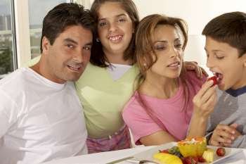 Portrait of a mid adult man with his daughter and mid adult woman feeding her son a strawberry