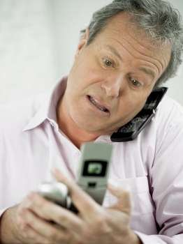 Close-up of a mature man talking on a mobile phone and holding two mobile phones in his other hand