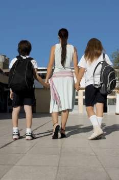 Rear view of a mid adult woman with her two children walking with holding hands