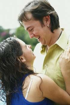Side profile of a young woman and a mid adult man embracing each other and smiling