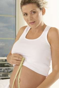 Portrait of a pregnant woman measuring her abdomen with a measuring tape