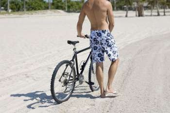 Rear view of a man standing and holding a bicycle on the beach