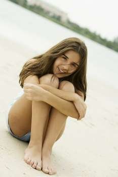 Portrait of a teenage girl sitting on the beach smiling