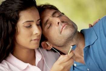 Mid adult man resting on a young woman´s shoulder and listening to music
