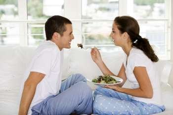 Side profile of a young woman feeding a young man salad