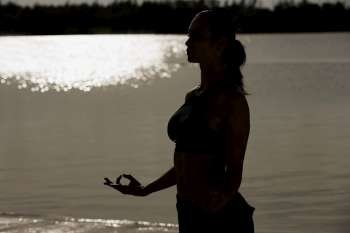 Silhouette of a mid adult woman meditating on the beach