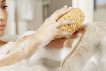 Close-up of a young woman using a bath sponge on her arm