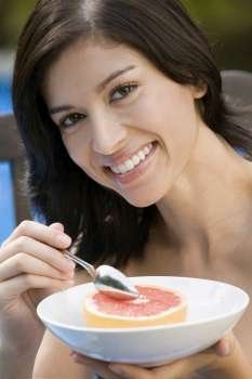 Portrait of a young woman eating grapefruit and smiling
