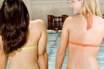 Rear view of two young women sitting at the edge of a swimming pool