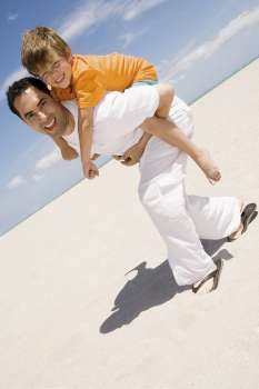 Portrait of a boy riding piggyback on his father on the beach