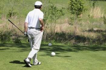 Rear view of a man holding a golf club and walking on a golf course