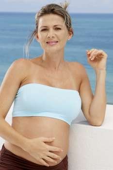 Close-up of a pregnant mid adult woman leaning against a wall with her hand on her abdomen