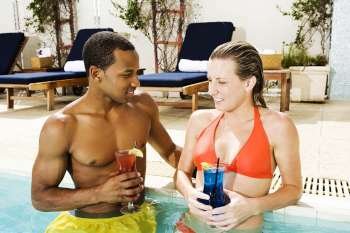Close-up of a young couple holding glasses in a swimming pool