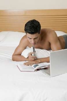 Young man lying on the bed holding a dictaphone with a laptop in front of him