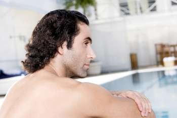 Rear view of a mid adult man sitting at the poolside