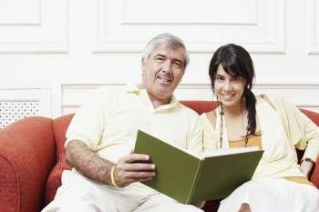 Portrait of a mature man sitting with his daughter on a couch and holding a book