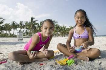 Portrait of two girls sitting on the beach and playing with sand