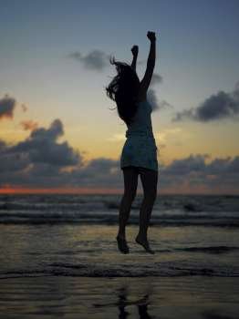 Silhouette of a teenage girl jumping on the beach at dusk