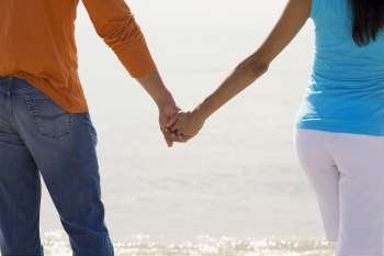 Mid section view of a young couple standing on the beach and holding hands