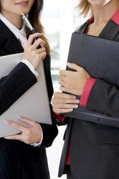 Close-up of two businesswomen holding a file and a laptop