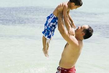 Side profile of a mid adult man picking up his son in water