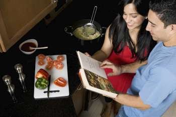 High angle view of a couple preparing food with the help of a cookbook in the kitchen