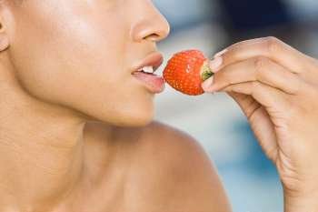 Close-up of a young woman holding a strawberry close to her mouth