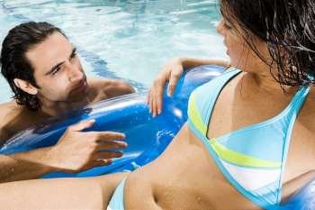 Close-up of a young woman and a mid adult man looking at each other in a swimming pool