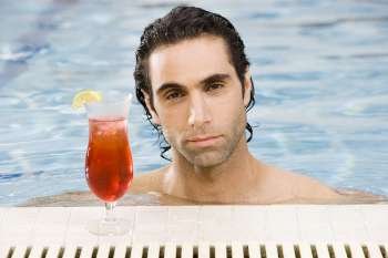 Portrait of a mid adult man in a swimming pool with a cocktail