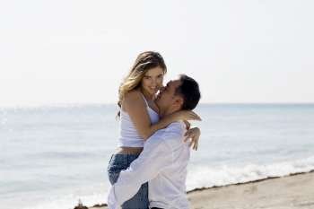 Side profile of a mid adult man lifting a young woman on the beach