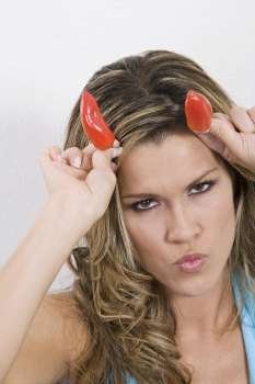 Portrait of a young woman putting two red chili peppers on her head