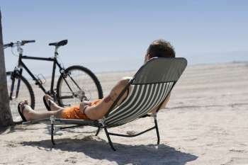 Rear view of a man reclining on a lounge chair on the beach