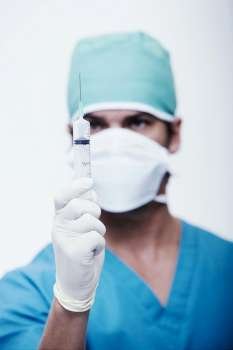 Close-up of a surgeon in scrubs holding a syringe