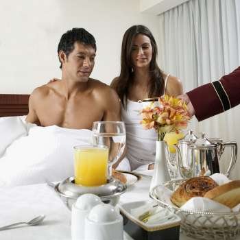Person´s hand serving tea to a young woman and a mid adult man on the bed