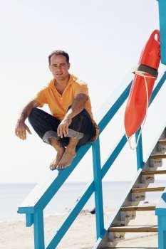 Portrait of a mid adult man sitting on the hand rail of a lifeguard hut and smiling