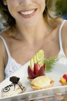 Close-up of a young woman holding assorted tarts with an eclair in a platter
