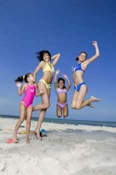 Two young women and two girls jumping on the beach