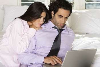 Close-up of a businessman and a businesswoman sitting on the bed using a laptop