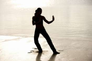 Silhouette of a young woman practicing martial arts on the beach