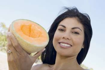 Portrait of a mid adult woman holding a half melon and smiling