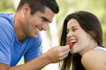 Side profile of a mid adult man feeding a young woman a strawberry