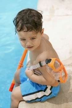 High angle view of a boy holding snorkel sitting by the pool