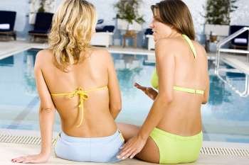 Rear view of two young women sitting on a bench at the poolside