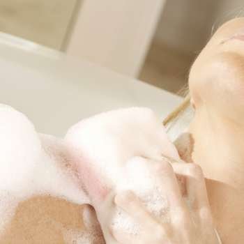 Close-up of a young woman scrubbing her shoulder with a bath sponge