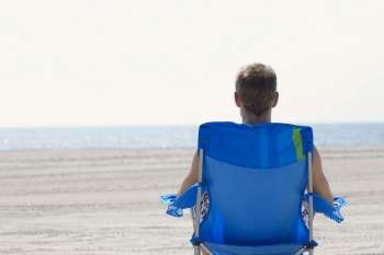 Rear view of a young man sitting on a lounge chair on the beach