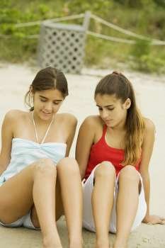 Two girls sitting in sand at the beach