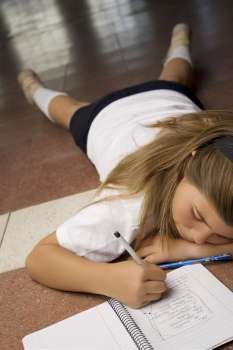 Schoolgirl lying on the floor and writing in a spiral notebook